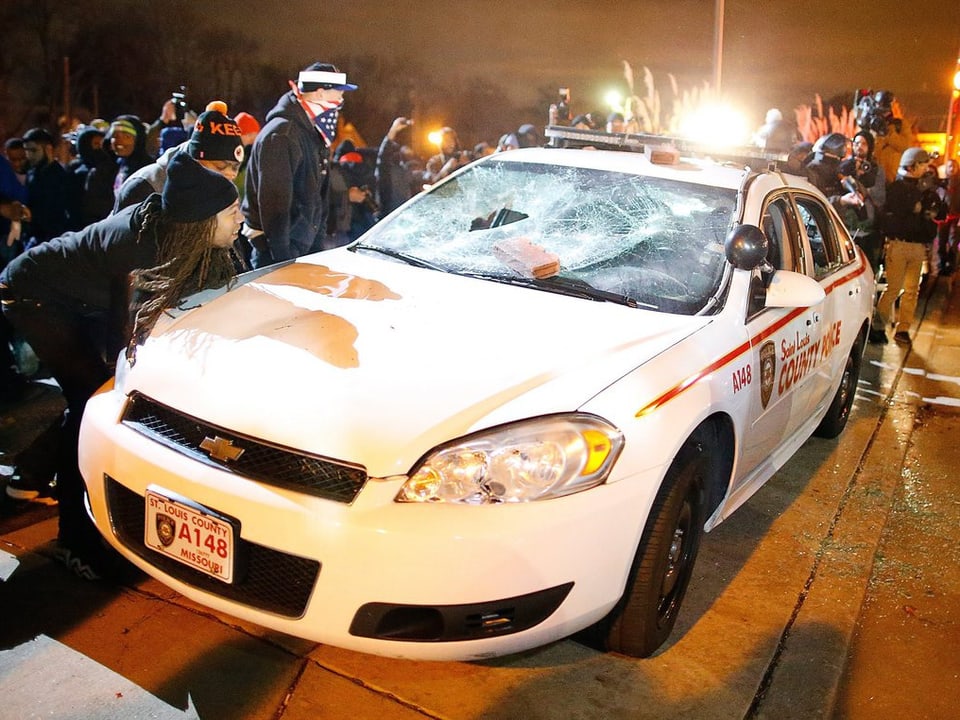 Demonstranten vor einem zerstörten Polizeiwagen