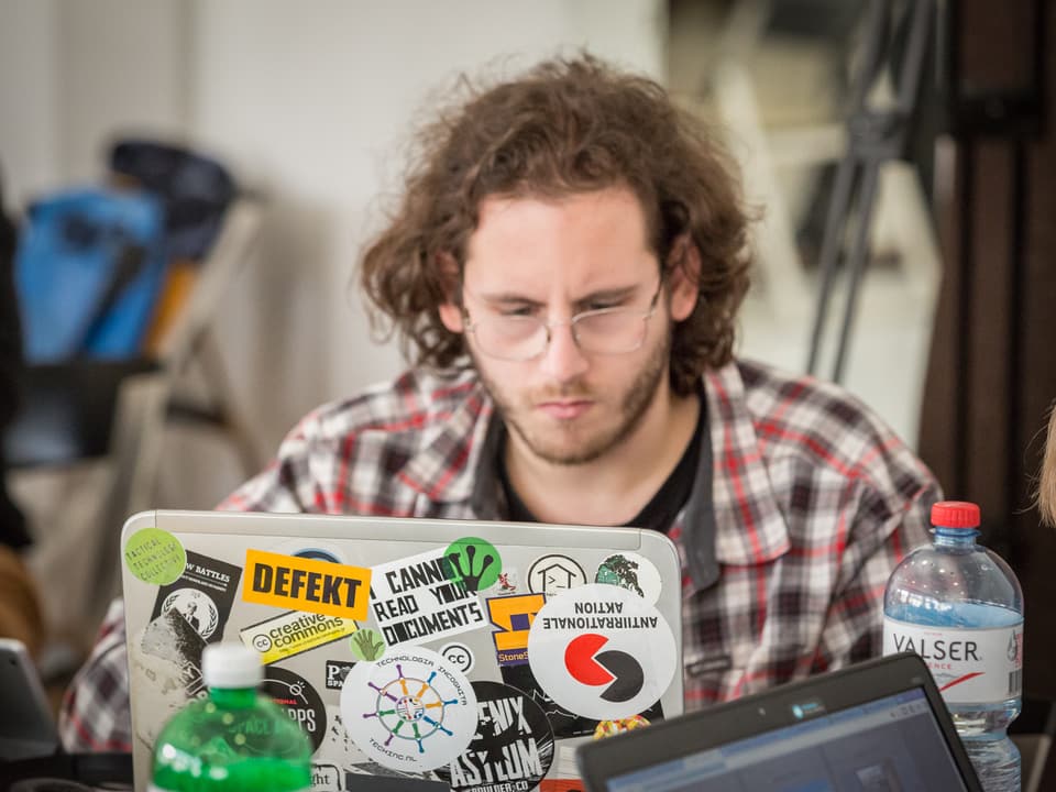 Ein Teilnehmer des Hackathons sitzt vor seinem Laptop, der mit bunten Aufklebern beklebt ist.