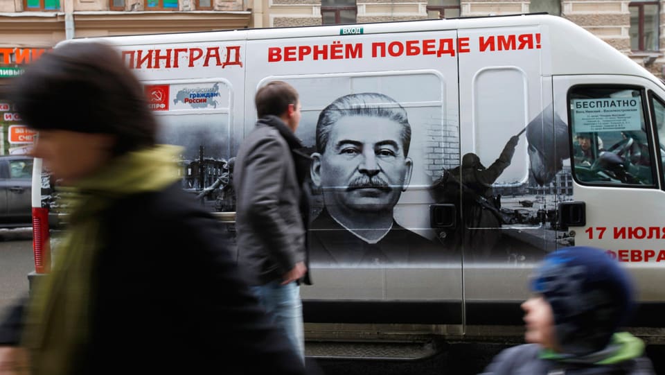 Ein weisser Bus, der auf der Seitentüre ein schwarz-weiss-Porträt von Stalin zeigt.