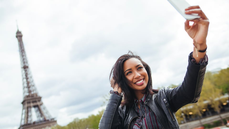 Eine junge Frau schiesst ein Selfie vor dem Eiffelturm. 