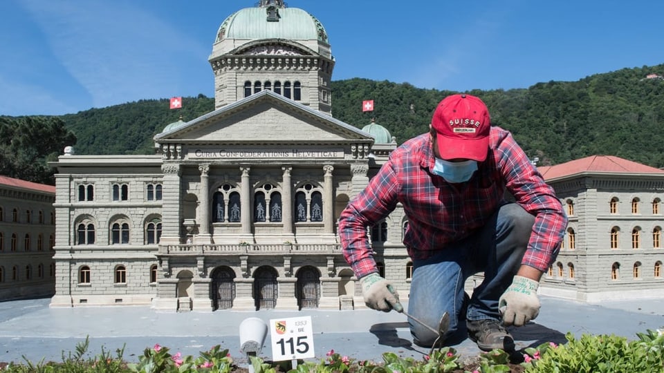 Mann beim Gärntern neben Modell des Bundeshauses