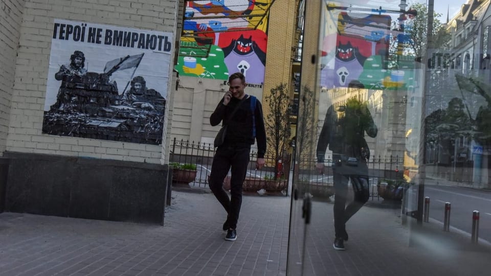 Plakat mit Kriegsparolen im Zentrum von Kiew, Mann am Handy