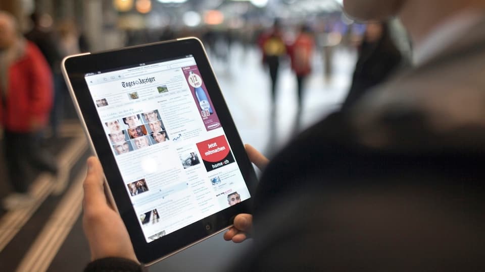 Mann liest im Bahnhof auf einem Tablet die Zeitung.