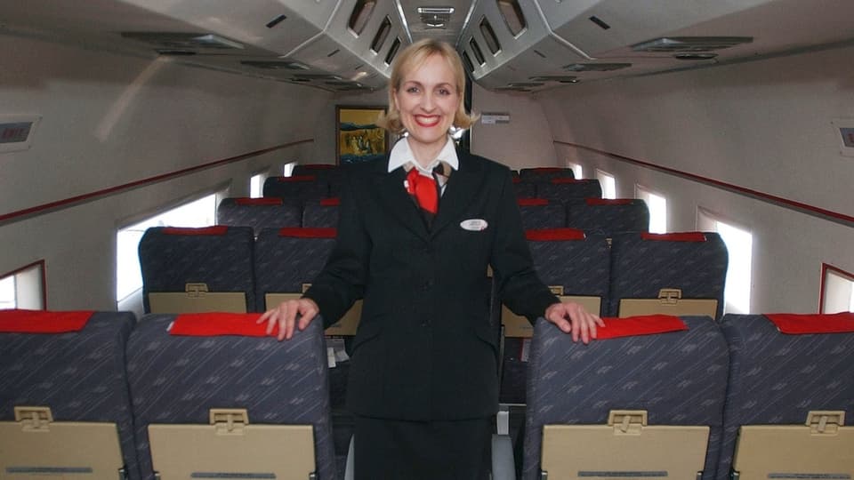 Frau in Uniform lächelt in einem leeren Flugzeug