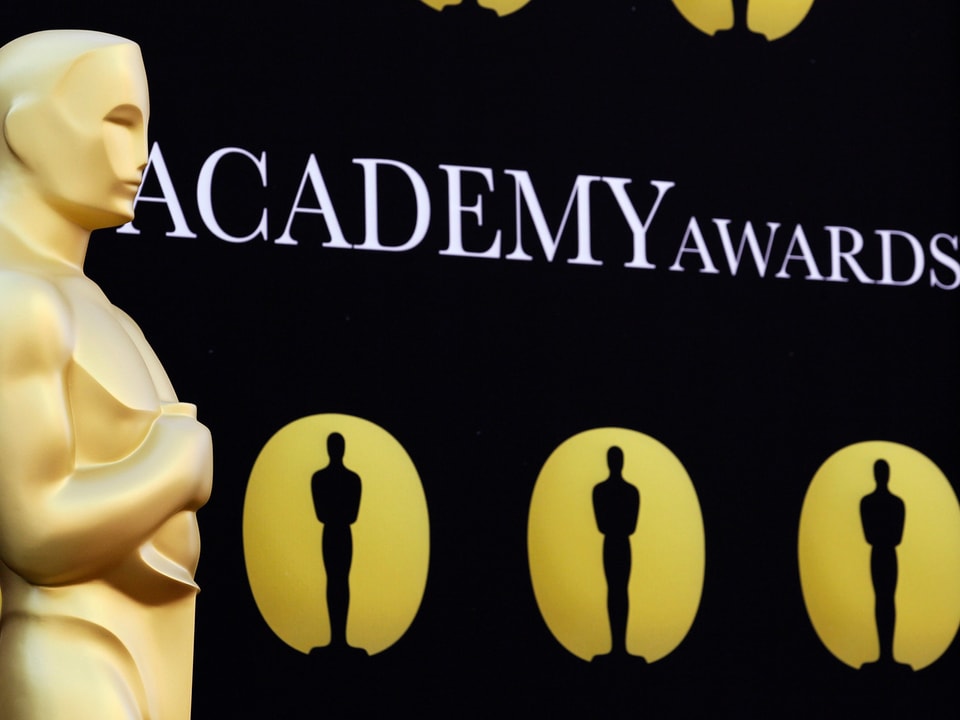 Eine Oscar-Statue im Vordergrund. Ein schwarzer Hintergrund mit der Aufschrift «Academy Awards».