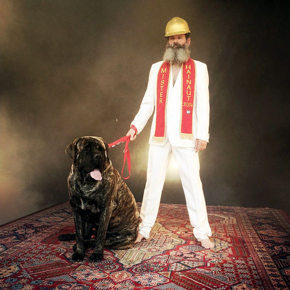 Mann in weissem Anzug mit goldenem Helm und grossem Hund steht auf fliegendem Perserteppich.