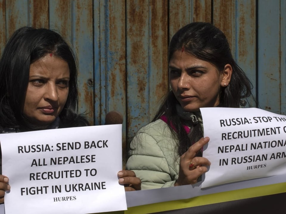 Zwei Frauen halten Protesttbotschaften in den Händen. Sie fordern von Russland, dass die Nepalesen zurückkehren.