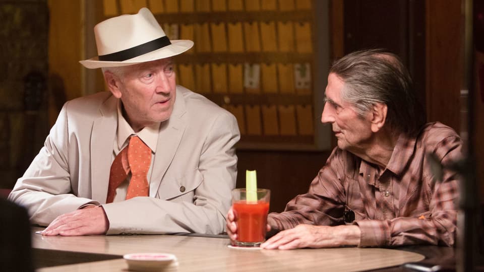 Filmszene: Zwei Männer sitzen an einer Bar und sprechen miteinander.