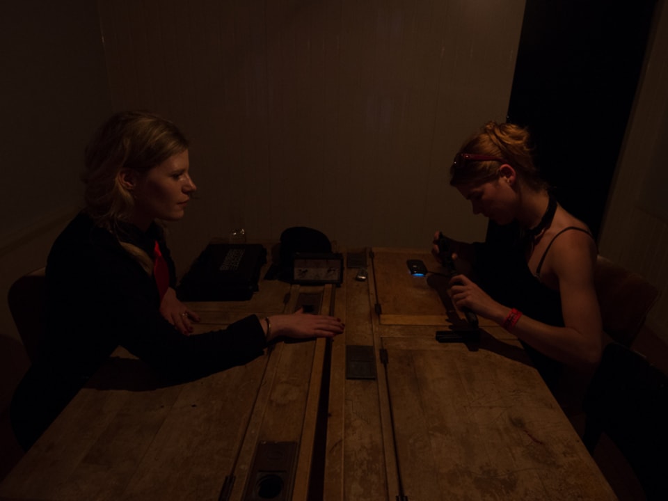 In der Dunkelheit kaum erkennbar sitzen zwei Frauen an einem Tisch und setzen eine Pistole zusammen.