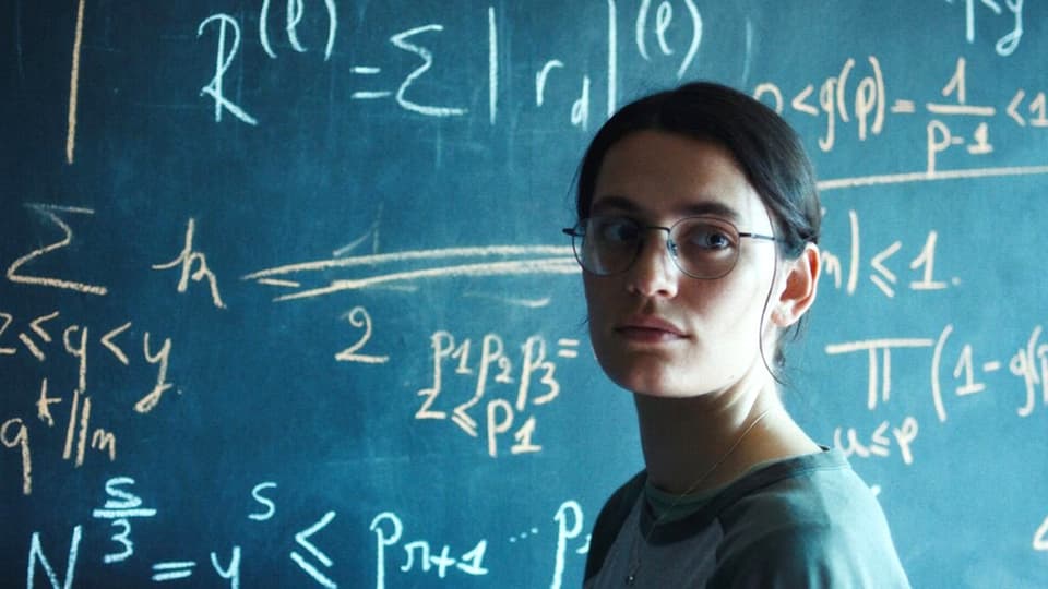 Eine junge Frau vor einer Wandtafel voller mathematischer Formeln.