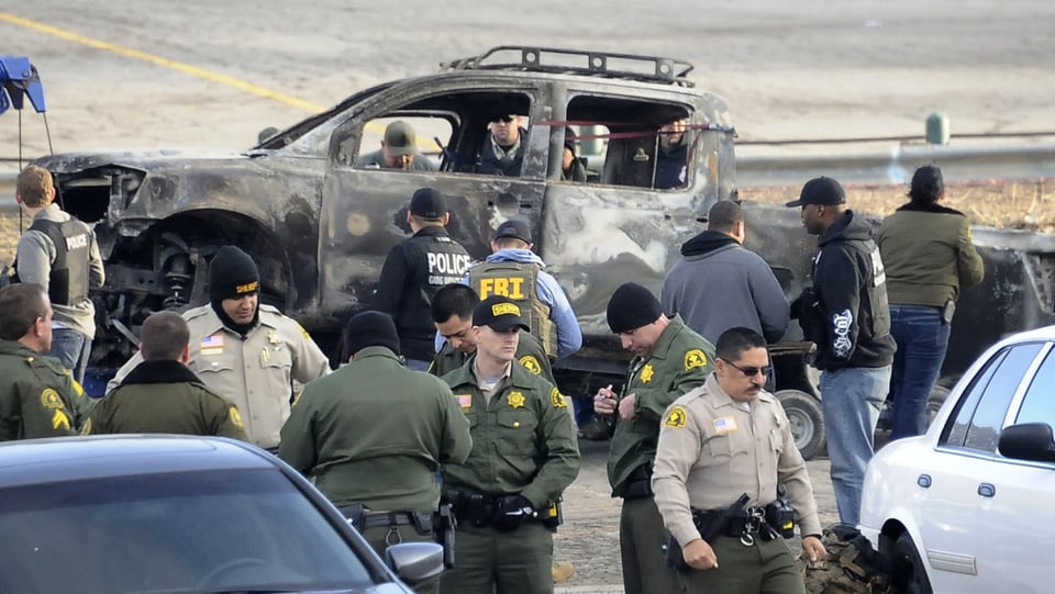 Polizisten neben dem ausgebrannten Auto des mutmasslichen Mörders