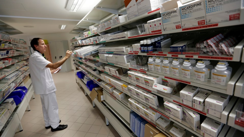 Ein Mann steht vor einerm mit Medikamenten gefüllten Regal. 