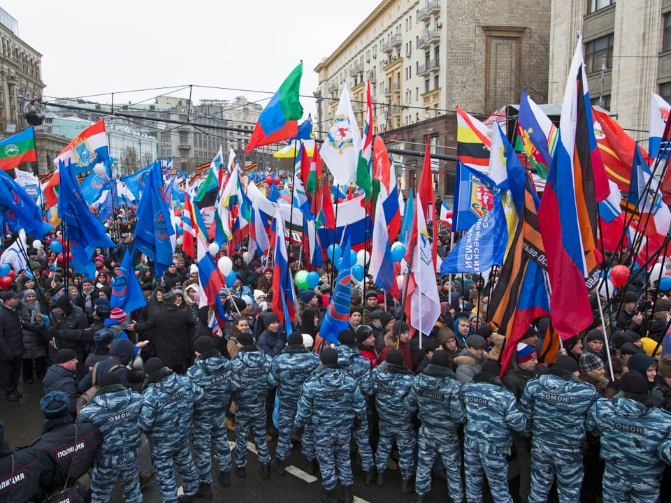 Russische Polizei und Militärs bilden einen Strassengang, Demonstranten laufen darin mit Fahnen.