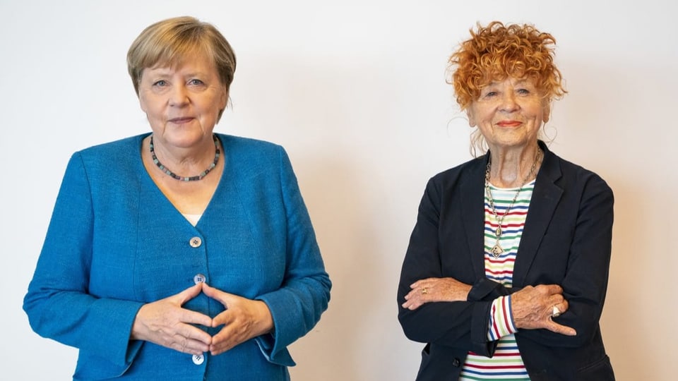 Frau in Anzug faltet die Hände zur Raute (Angela Merkel), neben ihr eine Frau mit rotgefärbten Haaren (Herlinde Koelbl)