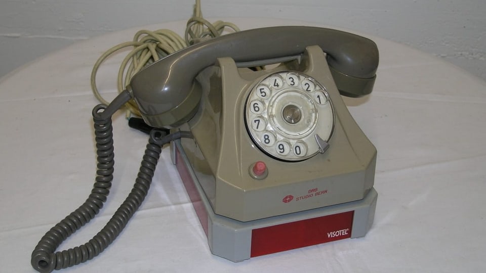 Ein altes graues Telefon mit Drehscheibe auf einem Tisch.