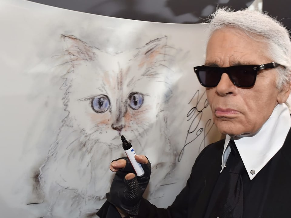 Karl Lagerfeld an einer Vernissage vor einer Zeichnung seiner Katze Choupette.
