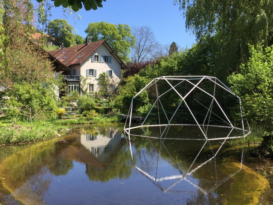 Skulptur schwimmt im Teich vor einem Haus. 