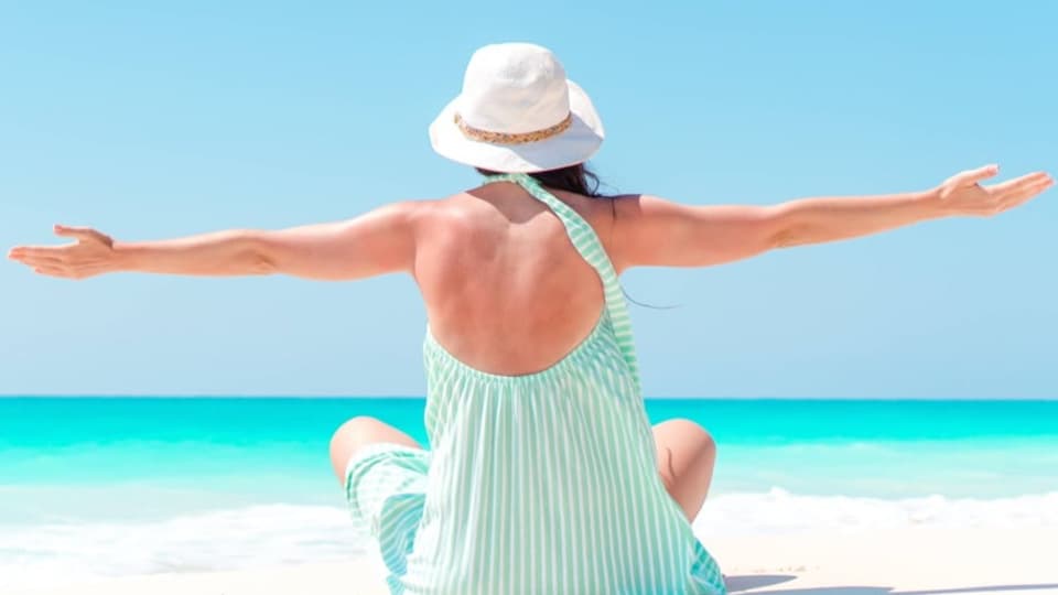 Eine Frau mit ausgebreiteten Armen sitzt am Strand in der Karibik.