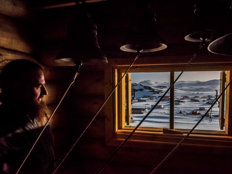 Mann schaut aus Hütte durch Fenster auf verschneite Landschaft