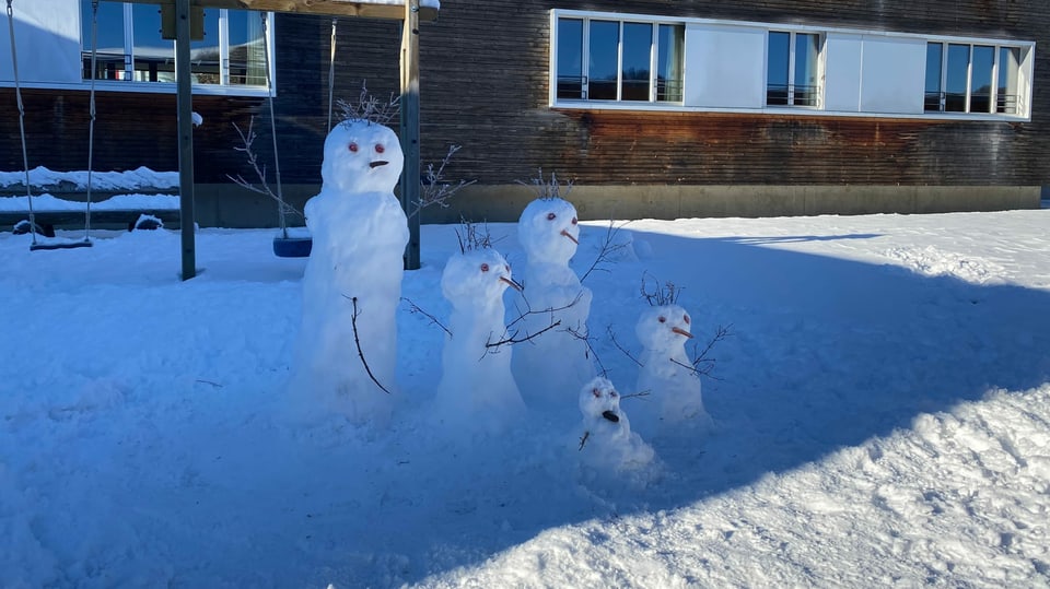 Fünf Schneemänner stehen vor einem Haus.