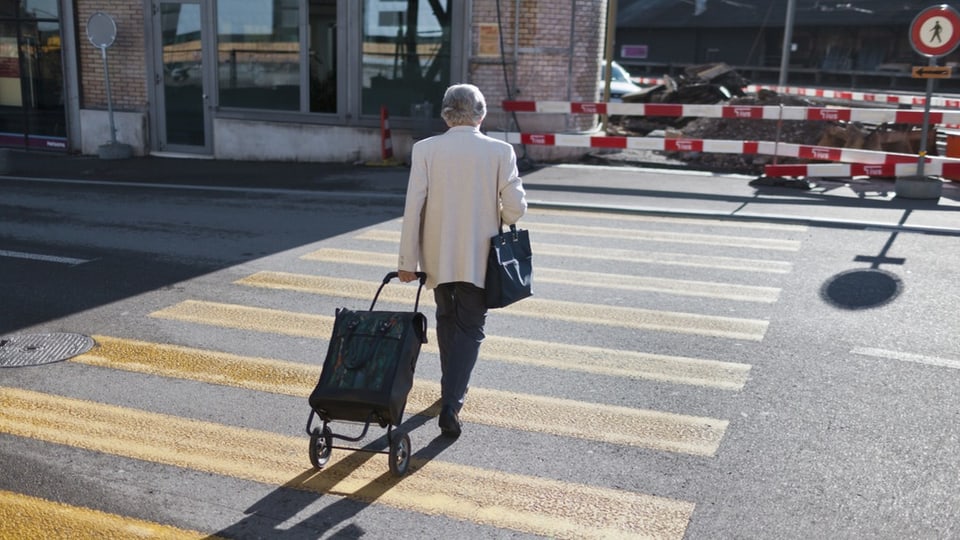 Eine ältere Frau läuft mit ihrem Einkaufswagen über den Fussgängerstreifen. 