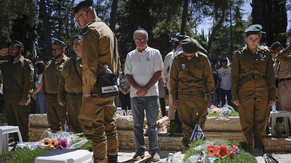Soldaten und Zivilpersonen vor jüdischen Gräbern mit gesenkten Haupt.