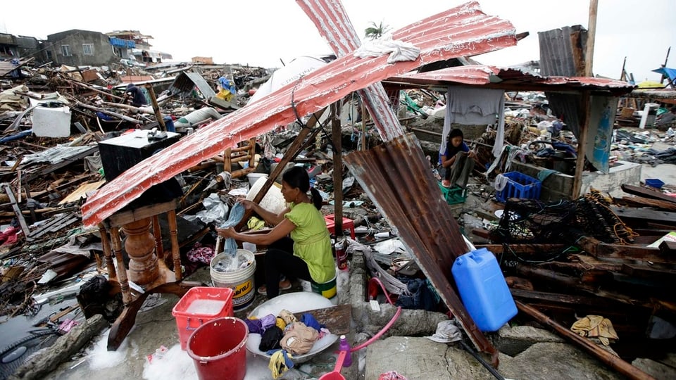 Eine Frau sitzt in einer vollständig zerstörten Siedlung und macht ihre Wäsche.
