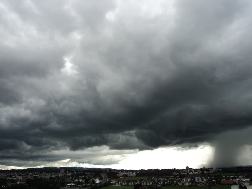 Viele graue Wolken, rechts am Bildrand ist der dunkle Vorhang eines Regenschauers zu sehen. Unten ganz klein noch der Stadtrand von Luzern. 