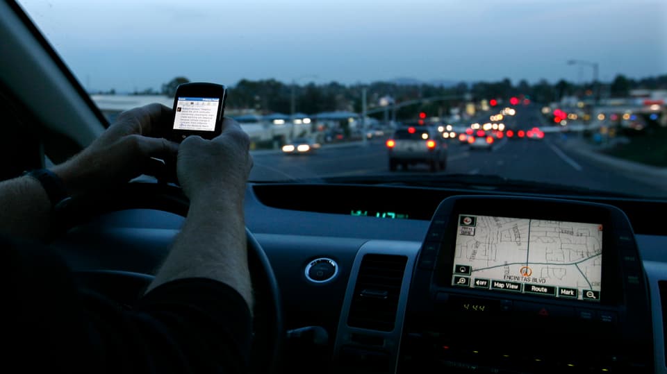 Jemand bedient ein Smartphone während des Fahrens, das Navigationsgerät leuchtet in der Dämmerung.
