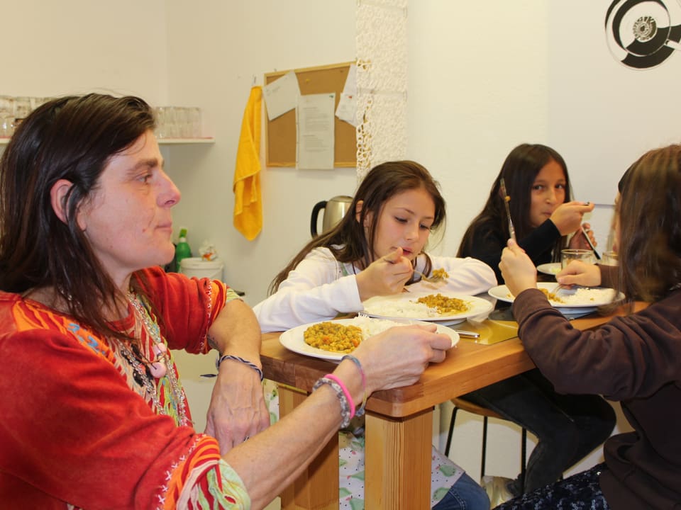 Eine Frau sitzt mit Mädchen an einem Tisch und isst.