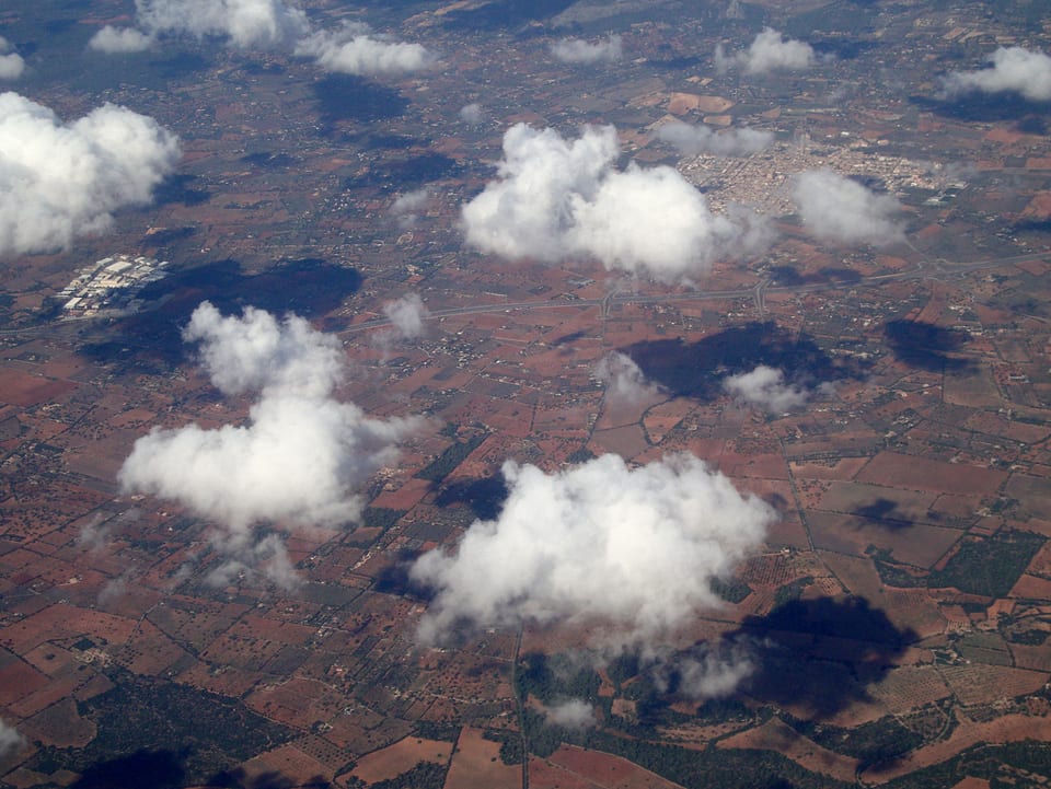 Blick aus dem Flugzeug auf die Landschaft und einige Wolken.