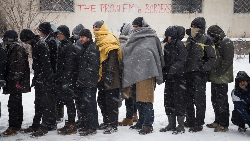 Männer stehen in einer Reihe im Schneetreiben, einige sind mit Wolldecken vermummt.
