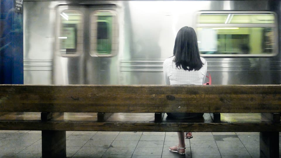 Eine Frau wartet auf einer Bank. Sie scheint auf die U-Bahn zu warten.