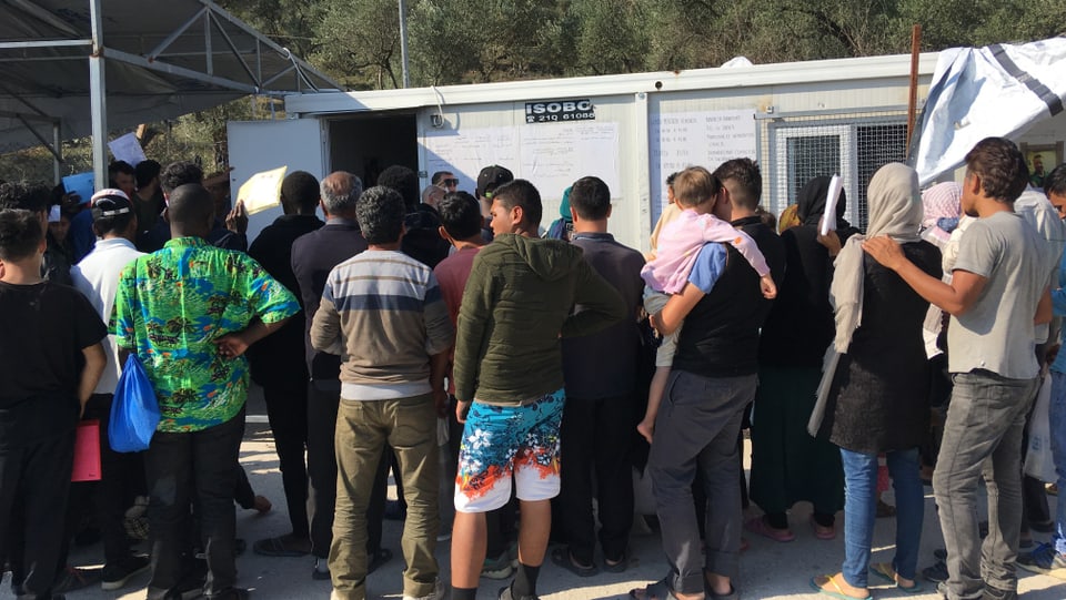 Mehrer Menschen stehen vor einem Gebäude in einem Flüchtlingscamp an.
