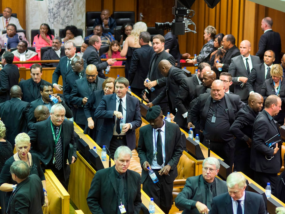 Parlamentarier in dunklen Anzügen gehen aus dem Saal