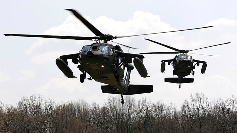 Zwei amerikanische Kampfhelikopter schweben über Buschland.