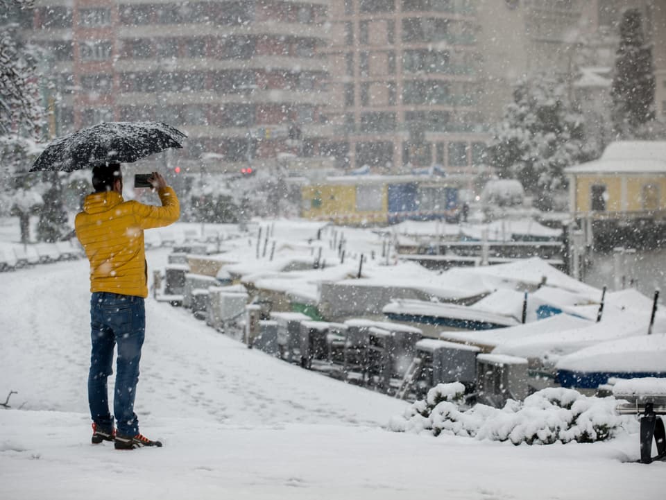 Ein Mann unter einem Schirm fotografiert das Schneegestoeber am Ufer des Luganersees