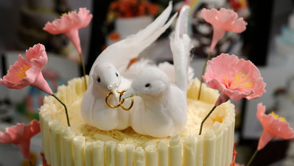 Hochzeitstorte mit zwei Tauben, die Eheringe in den Schnäbeln halten. 