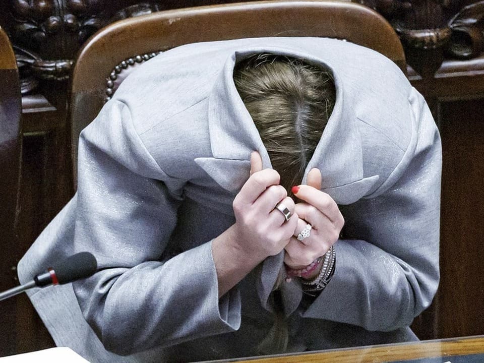 Giorgia Meloni verdeckt im Parlament ihren Kopf unter ihrem Blazer.