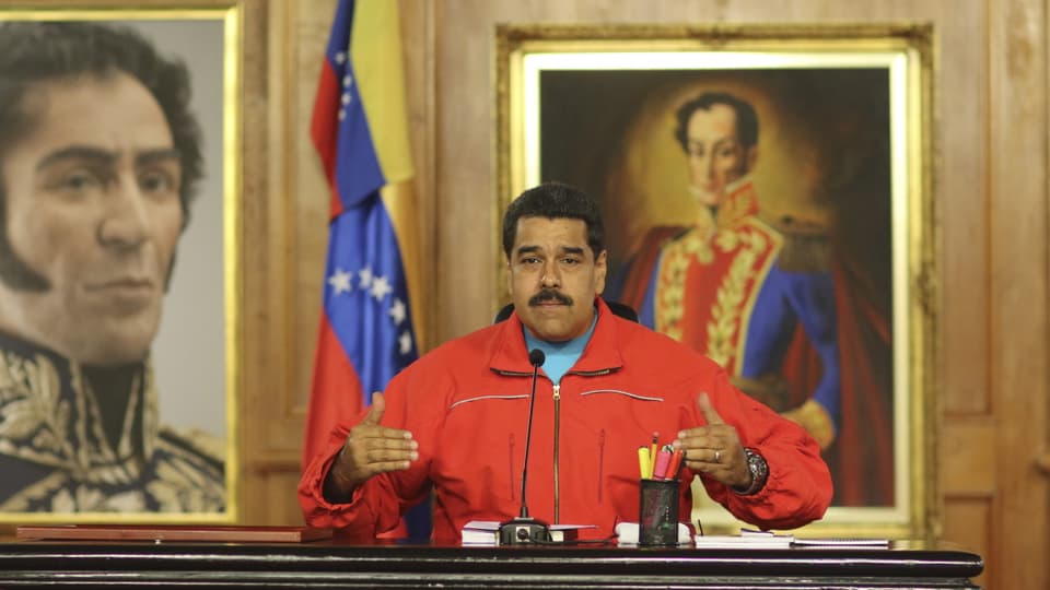 Der venezolanische Präsident Nicolás Maduro sitzt an einem Tisch und spricht in ein Mikrofon.
