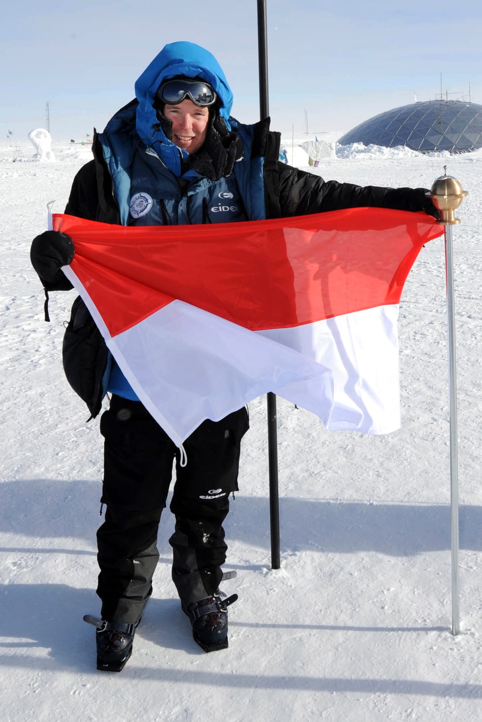 Fürst Albert dick eingepackt mit der Monaco-Flagge in der Hand am Südpol