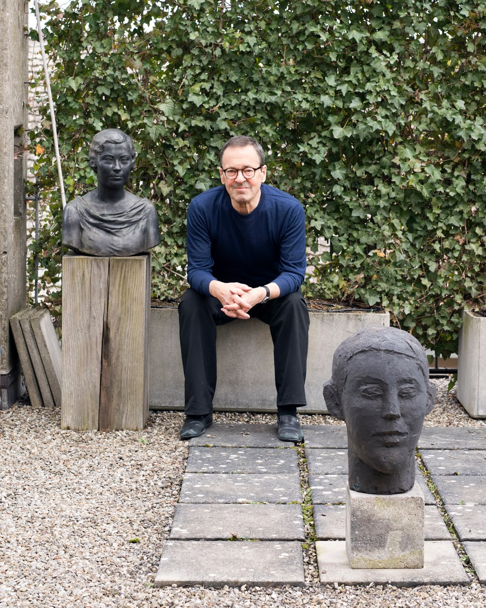 Martin Steinmann, zwischen draussen zwei Skulpturen auf einer Mauer sitzend.