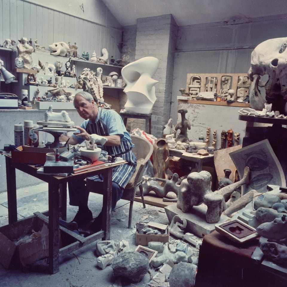 Henry Moore in seinem Atelier. Er modelliert. Der Raum ist voll mit Skulpturen.