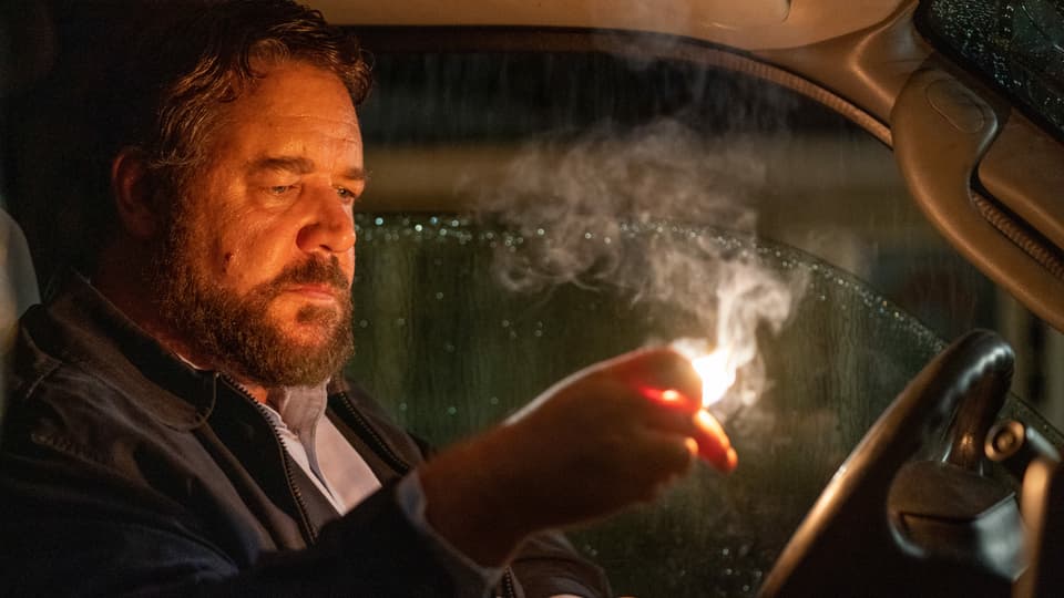 "Der Mann" (Russell Crowe) sitz am Steuer seines Autos und hält einen brennenden Zettel in der Hand.
