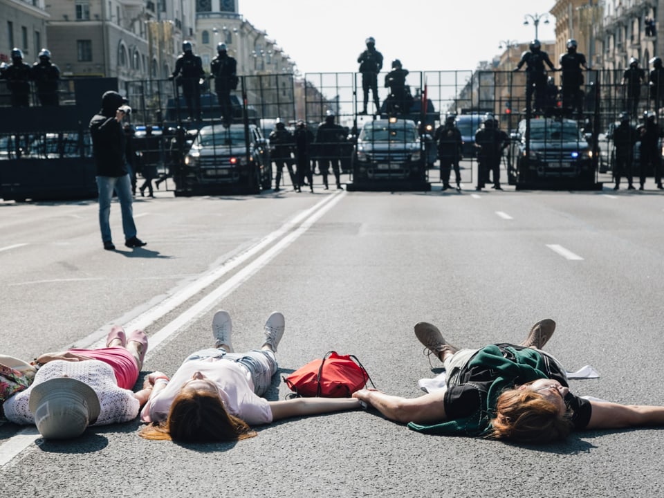 Drei Frauen liegen auf der Strasse - vor ihnen eine militärische Absperrung