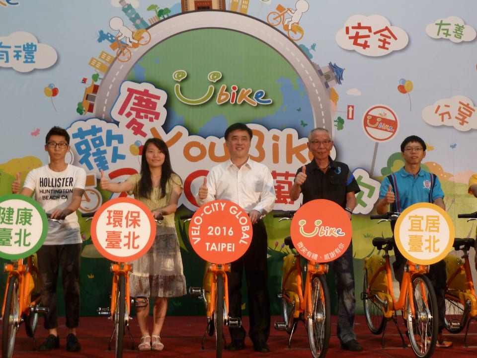 Auf einer Bühne stehen 5 Menschen mit erhobenem Daumen neben einem Velo  mit Aufschrift, dahinter das Youbike-Logo.