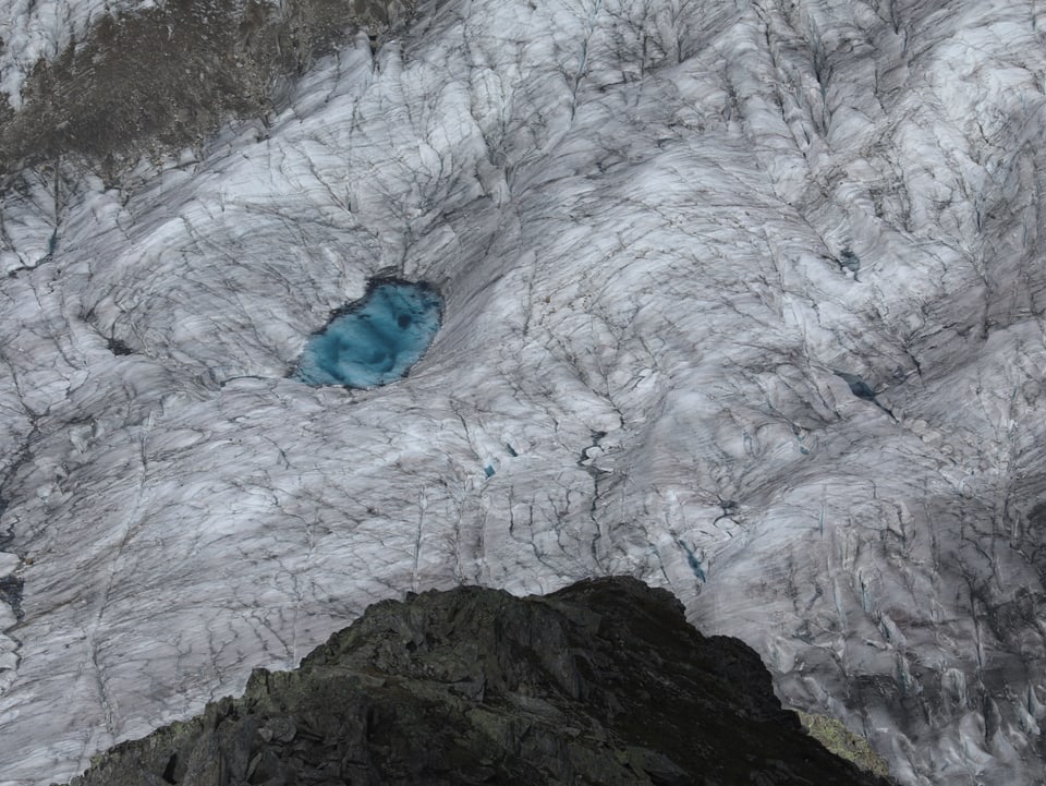 Aufnahme von oben auf einen Gletscher mit einem kleinen blauen Seelein. 