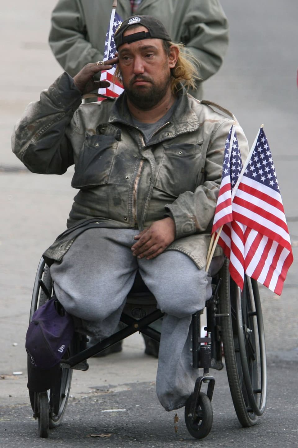 Ein Soldat auf einem Rollstuhl sitzend, beide Beine fehlen, salutiert.