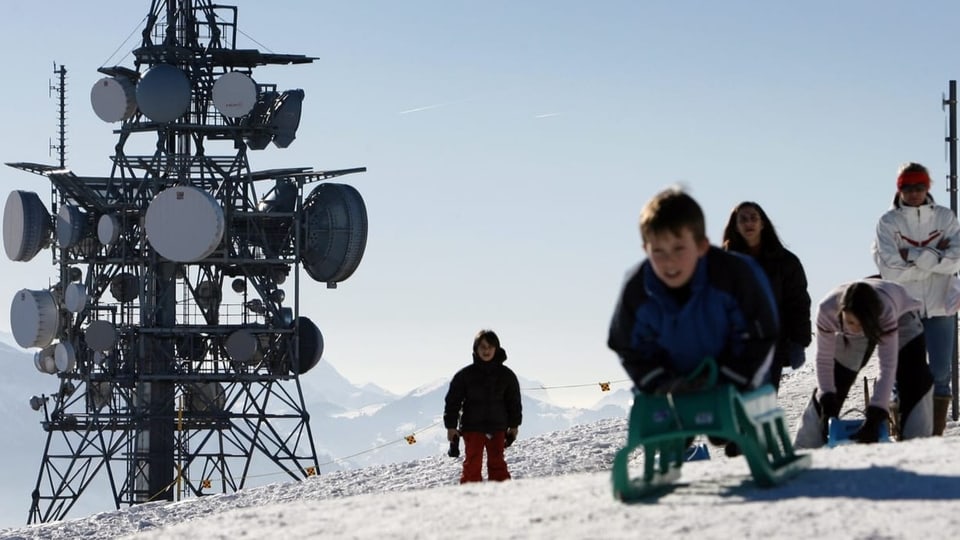 Kinder schlittlen auf dem Niederhorn, im Hintergrund eine riesige Sendeantenne