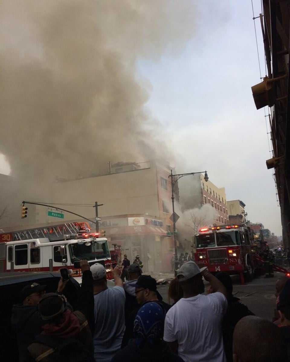 Weisser Rauch steigt über einem Gebäude auf, davor stehen zwei Fahrzeuge der Feuerwehr.